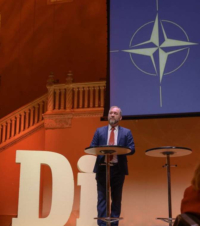 Freddy Jönsson Hanberg på scen. Dagens Industri och Natos logotyp i bakgrunden.
