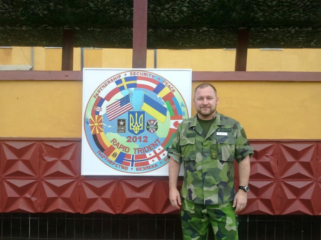 Freddy Jönsson Hanberg i kamouflagemönstrad dräkt framför skylt "2012 Rapid Trident".